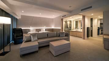 Una habitación de hotel moderna con un sofá grande, un pequeño otoman y una zona de estar con una silla.