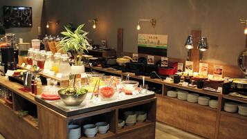 A buffet setup with various food items and beverages, including a plant centerpiece, in a well-lit room with wooden furniture and a sign indicating a local delicacy.