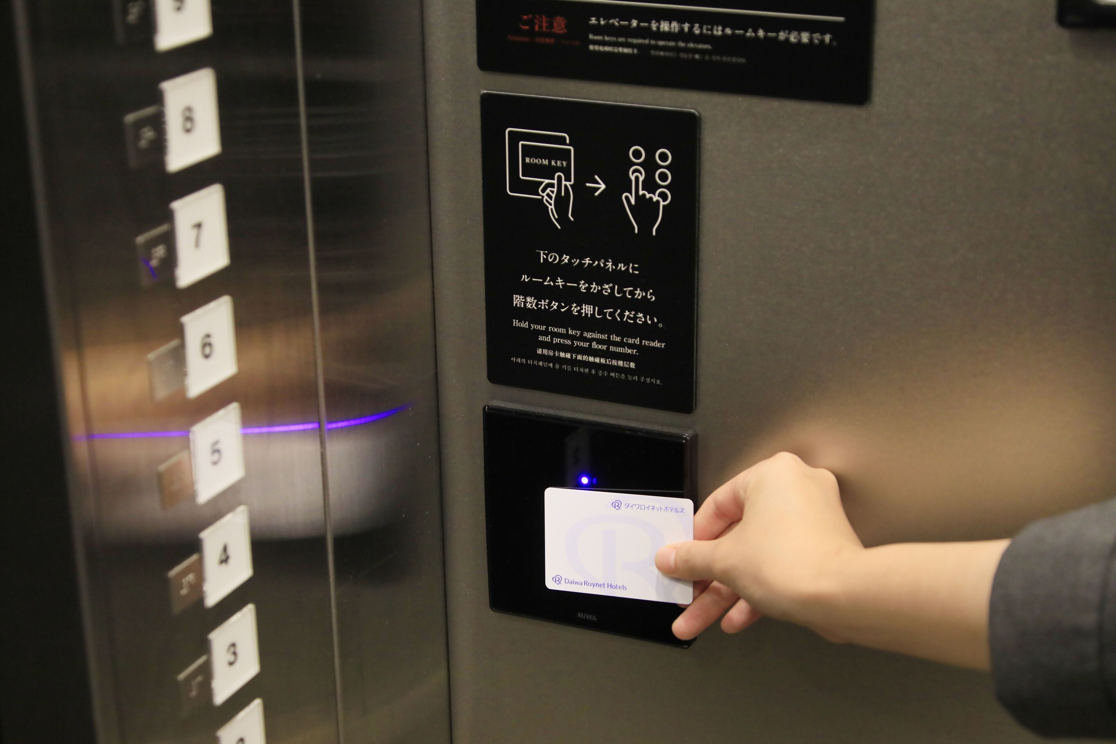 Un ascensor con lector de llave electrónica digital y una mano sosteniendo una tarjeta.
