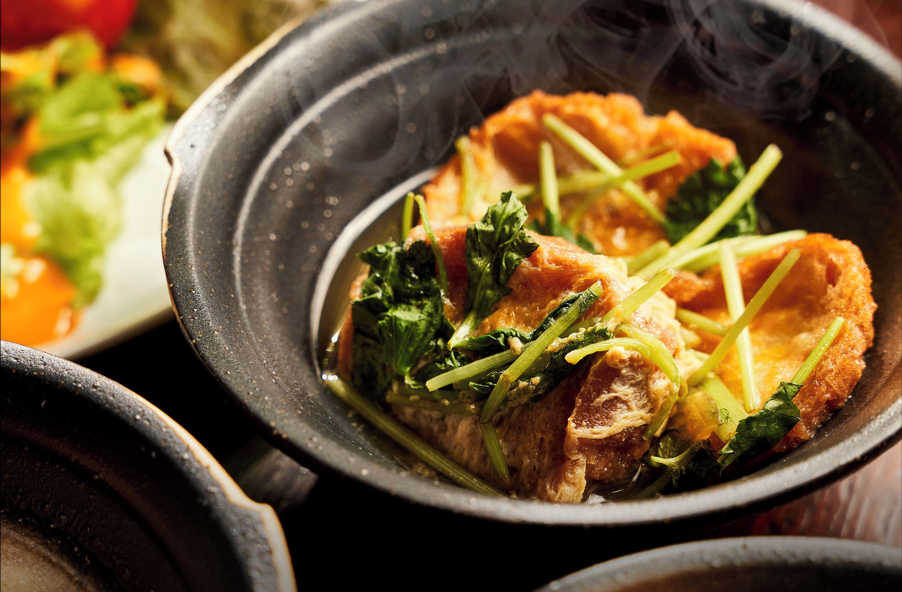 A close-up of a dish with salmon and greens in a black bowl.