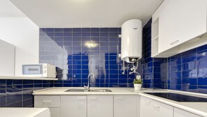 Une cuisine moderne avec des meubles blancs, un dosseret en carreaux bleus, un four à micro-ondes encastré et un chauffe-eau.