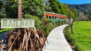 A wooden pathway leading to a green and orange train, with a 'RAILWAY' sign visible. - On The Track Lodge (Nydia Bay)
