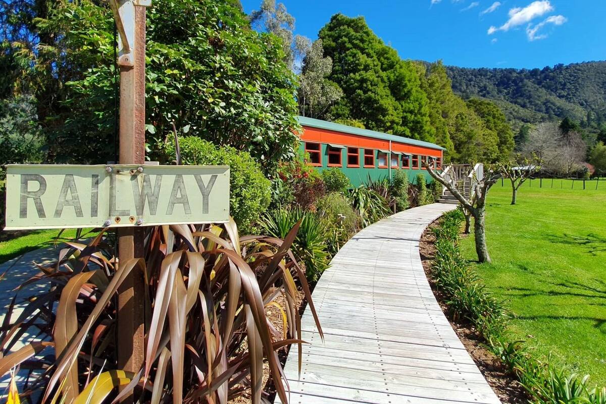 A wooden pathway leading to a green and orange train, with a 'RAILWAY' sign visible.