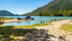 A lake with a boat docked on the shore, surrounded by lush green hills. - On The Track Lodge (Nydia Bay)