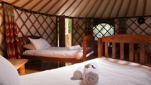 A cozy interior of a yurt with a bed, a wooden headboard, and a small table. - On The Track Lodge (Nydia Bay)