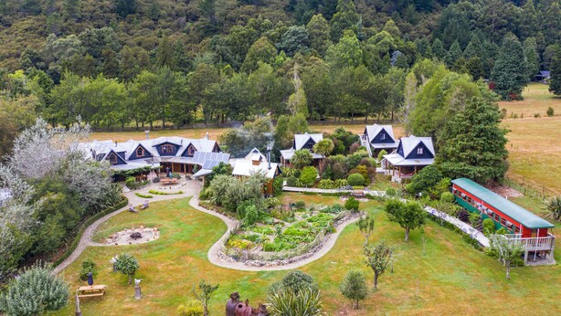 A cluster of houses with a central courtyard, surrounded by lush greenery and a forested backdrop. - On The Track Lodge (Nydia Bay)