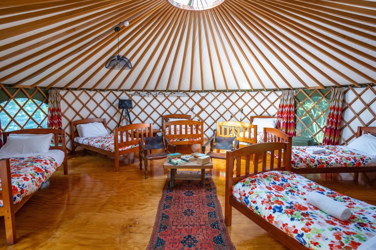A yurt with wooden beds, a central seating area, and a patterned rug.