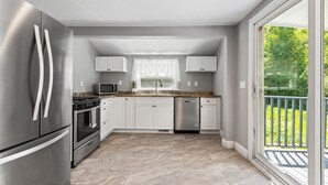 Een moderne keuken met roestvrijstalen apparatuur, witte kastjes en een grote schuifpui naar een balkon.