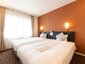 A hotel room with a large bed, two bedside lamps, a headboard with a control panel, and a window with curtains.