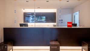 Een receptiebalie met een groot digitaal scherm, een rood bord en twee houten bankjes.