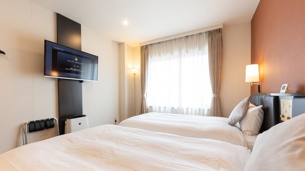 Hotelkamer met twee bedden, een wandtelevisie, een nachtkastje met lamp en een raam met gordijnen.