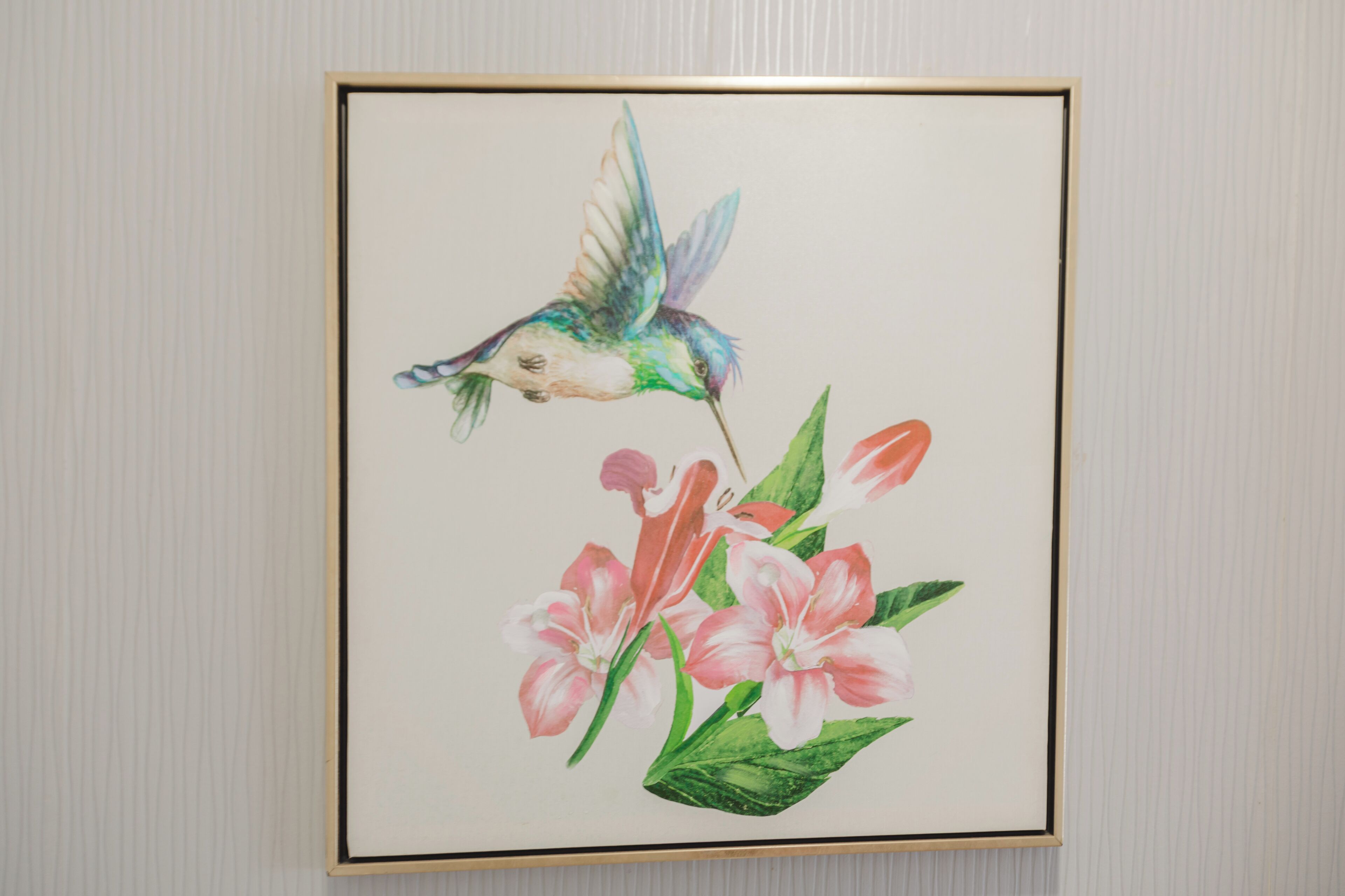 A framed artwork of a hummingbird and flowers on a wall.