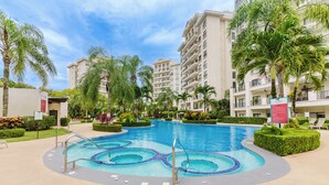 A swimming pool with a circular design, surrounded by palm trees and a multi-story building with balconies. - Lovely Mountain View Apartment (Jacó)