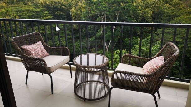 A balcony with wicker furniture and a glass table, overlooking a lush forested area. - Lovely Mountain View Apartment (Jacó)