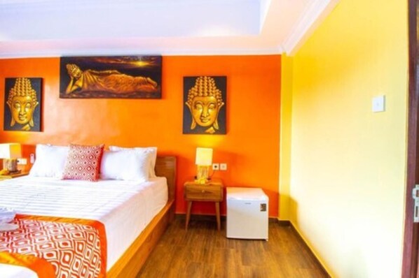Una habitación de hotel con cama, mesita de noche, lámpara y un pequeño electrodoméstico blanco.
