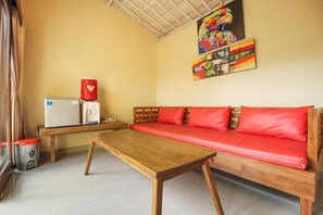 A room with a wooden sofa, a small wooden table, a refrigerator, and a trash bin.