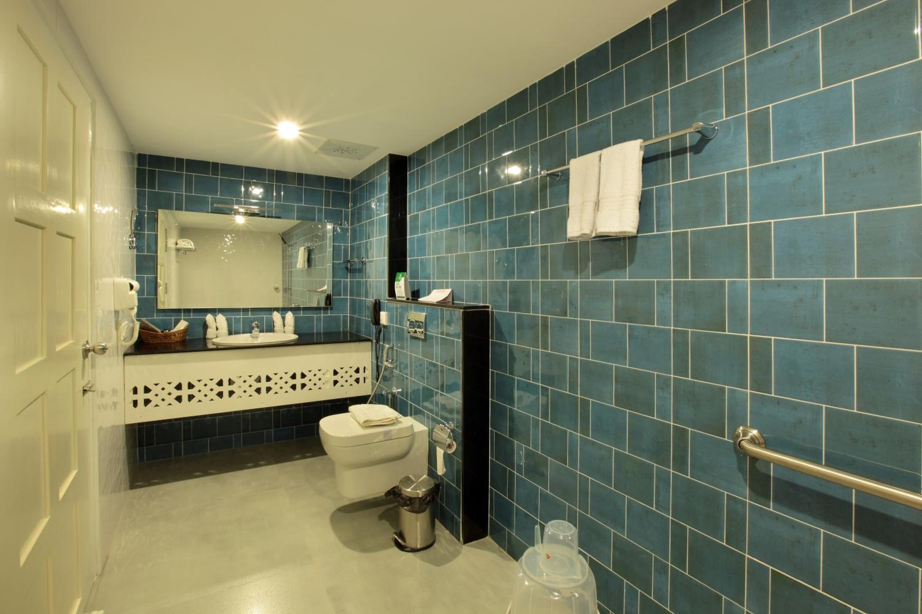 Ein Badezimmer mit blauen Fliesen, einer weißen Toilette, einem Waschbecken mit Spiegel und einem Handtuchhalter.