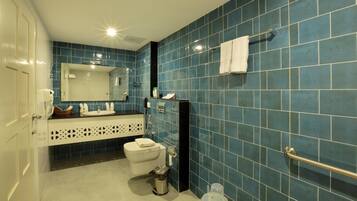 Ein Badezimmer mit blauen Fliesen, einer weißen Toilette, einem Waschbecken mit Spiegel und einem Handtuchhalter.