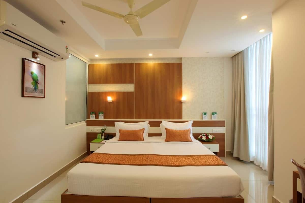 Quarto de hotel com cama, ventoinha no teto, espelho, mesa de cabeceira, luminária e janela com cortinas.