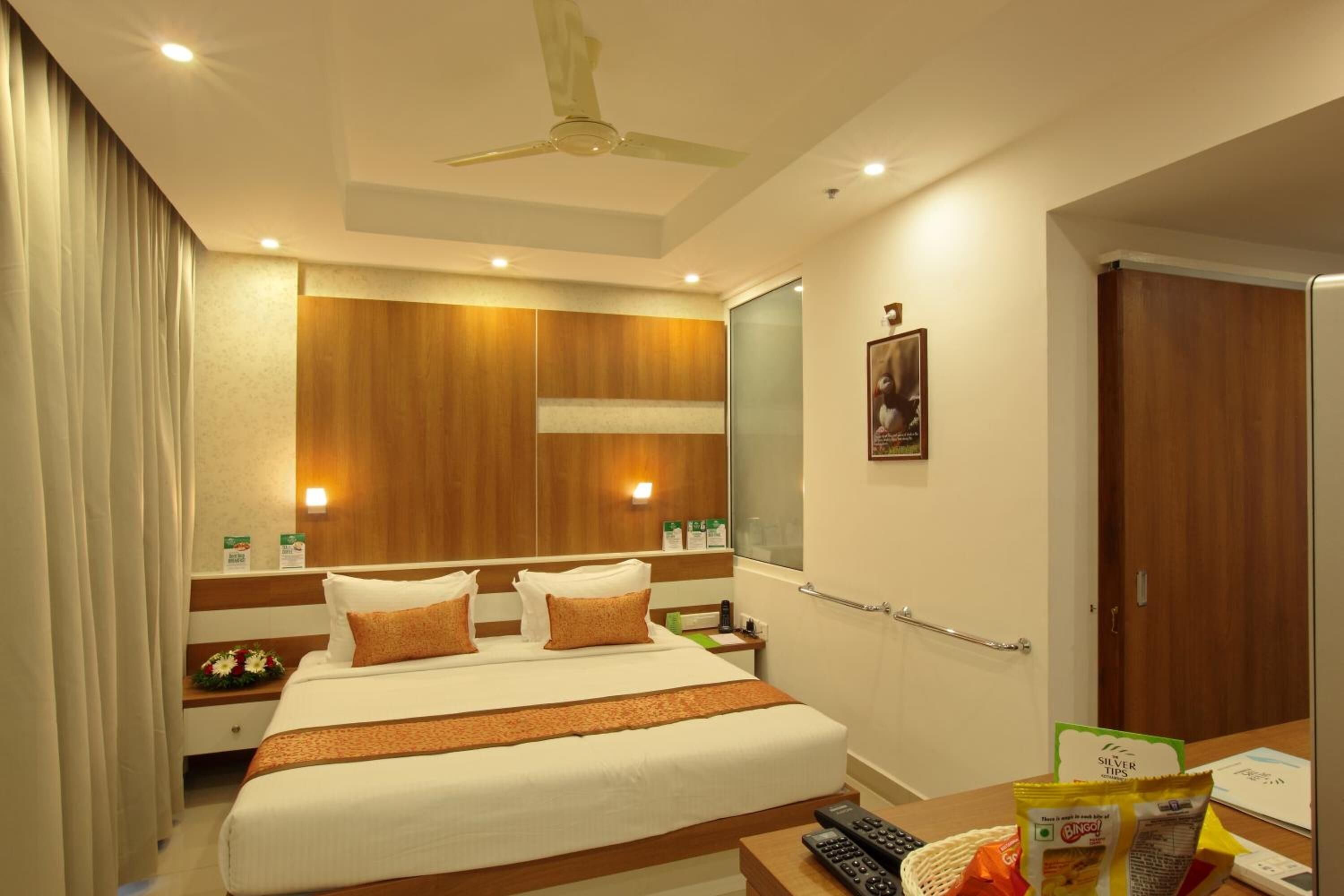 Een hotelkamer met een groot bed, een houten hoofdbord, nachtkastjes, een spiegel en een plafondventilator.