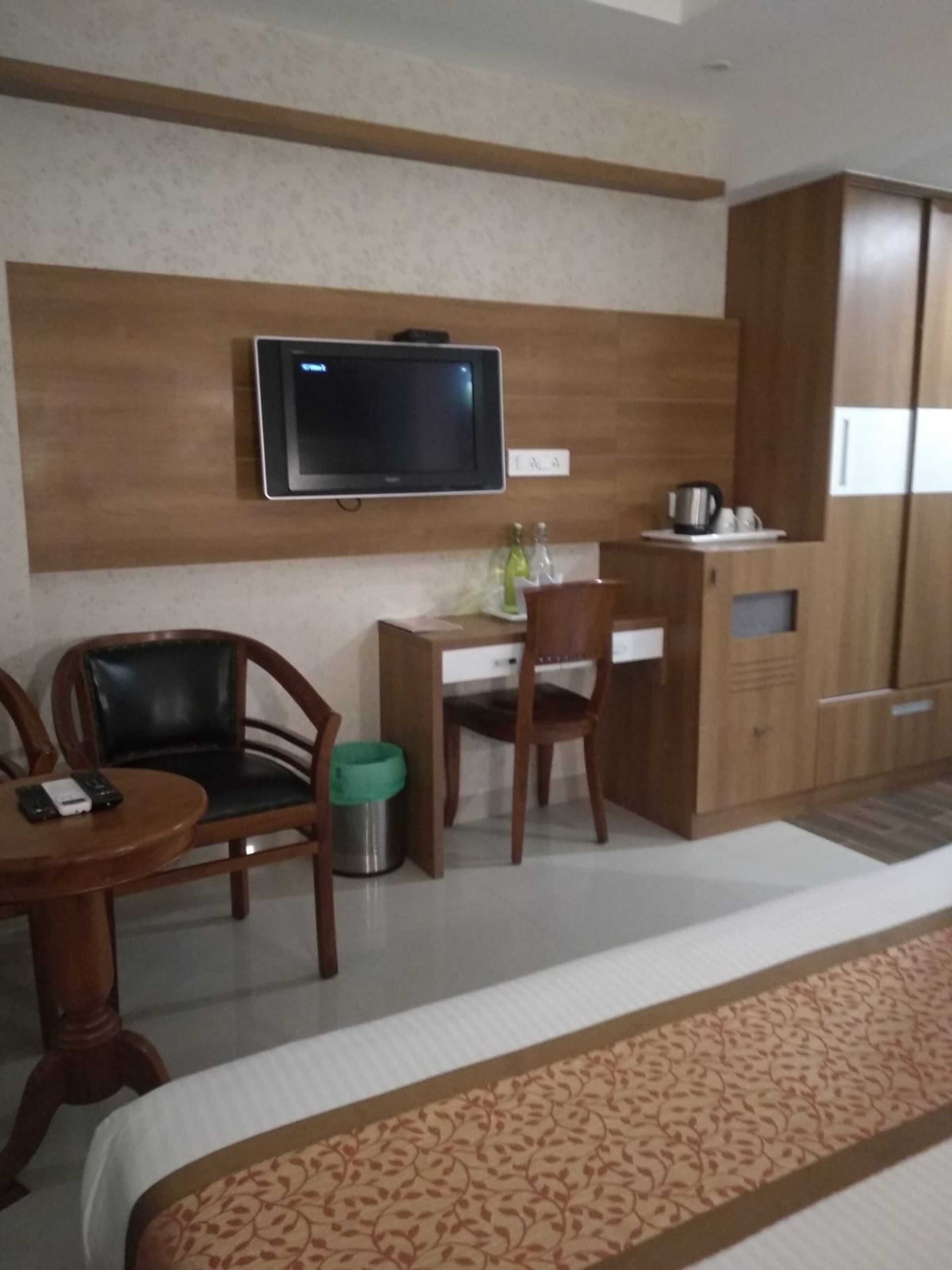 A hotel room with a bed, a desk with a chair, a television mounted on the wall, and a wardrobe.