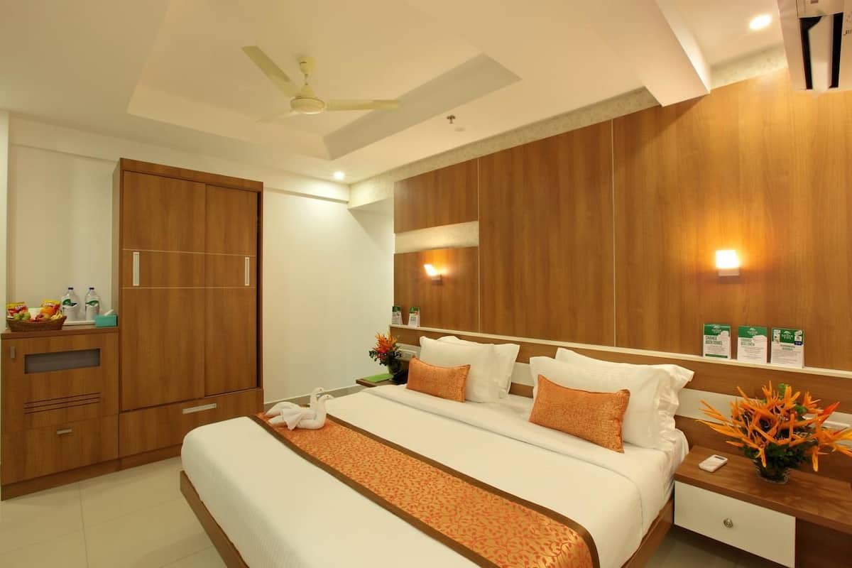 Quarto de hotel moderno com uma cama grande, guarda-roupa de madeira, mesa de cabeceira com um vaso e ventoinha no teto.