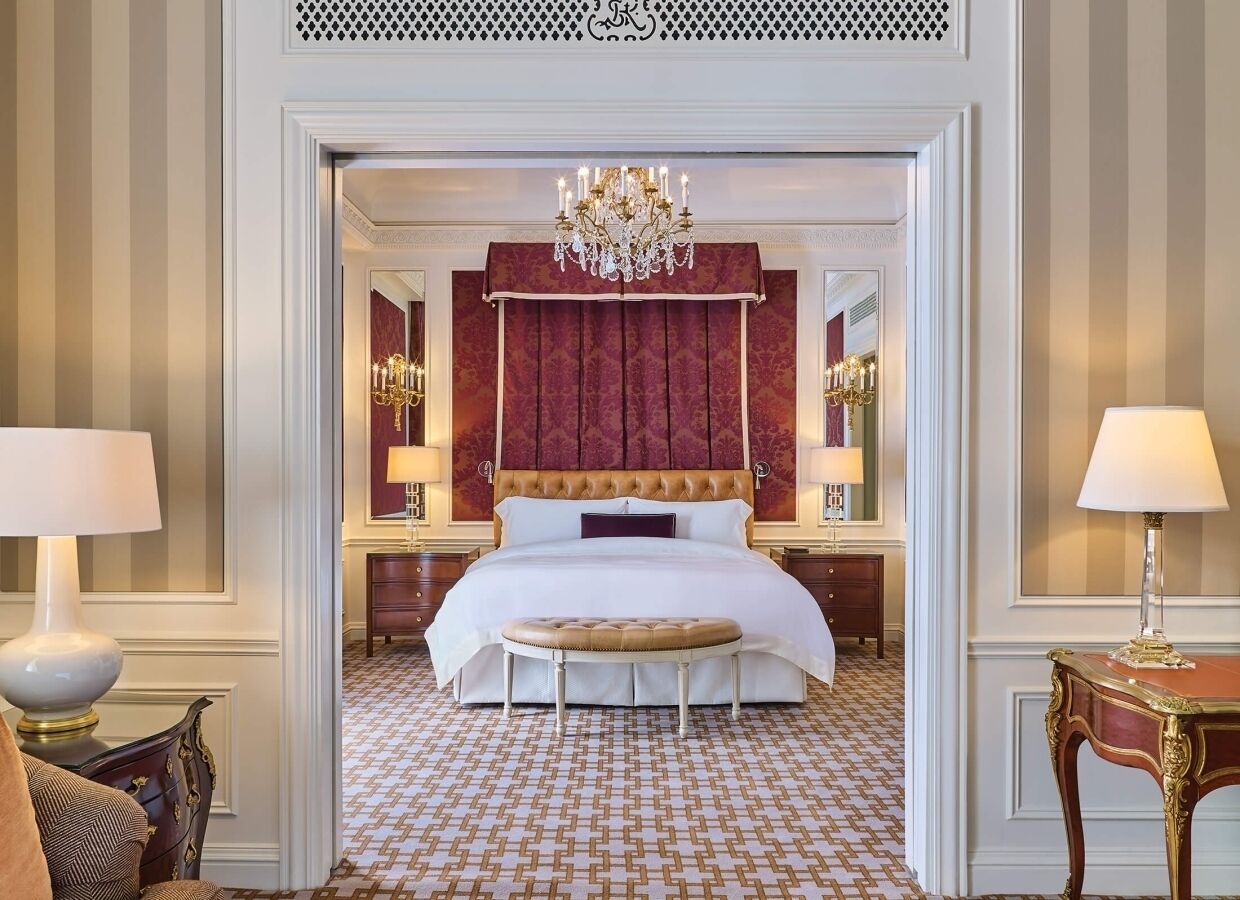 A hotel room with a large bed, a chandelier, a red headboard, and a patterned floor.