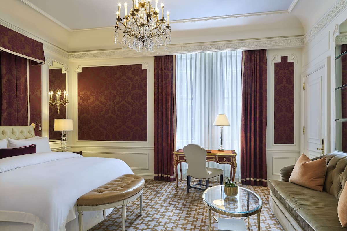 A hotel room with a large bed, a desk, a sofa, and a chandelier.