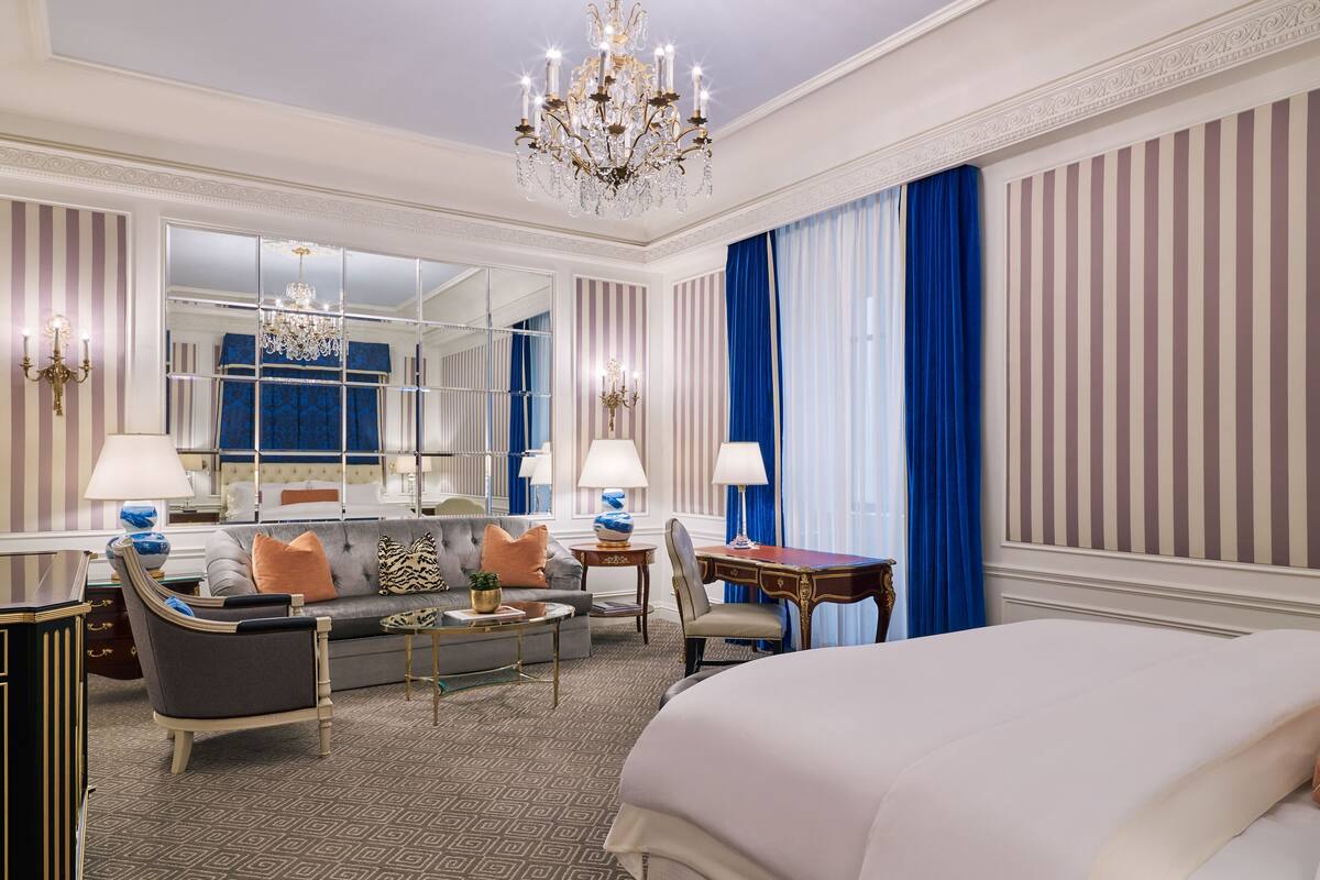 A hotel room with a large bed, a sofa, a coffee table, a desk, and a chandelier.