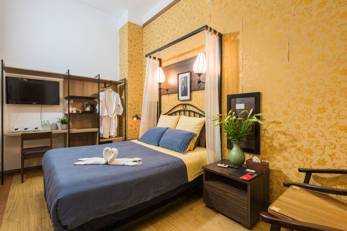A hotel room with a bed, bedside table, TV, desk, and wardrobe.