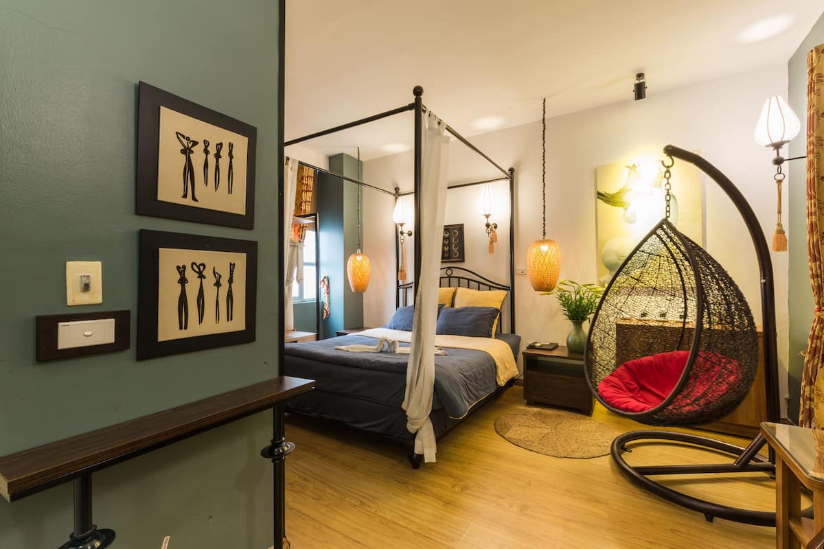 A four-poster bed with a canopy, a hanging chair, and artwork on the walls.