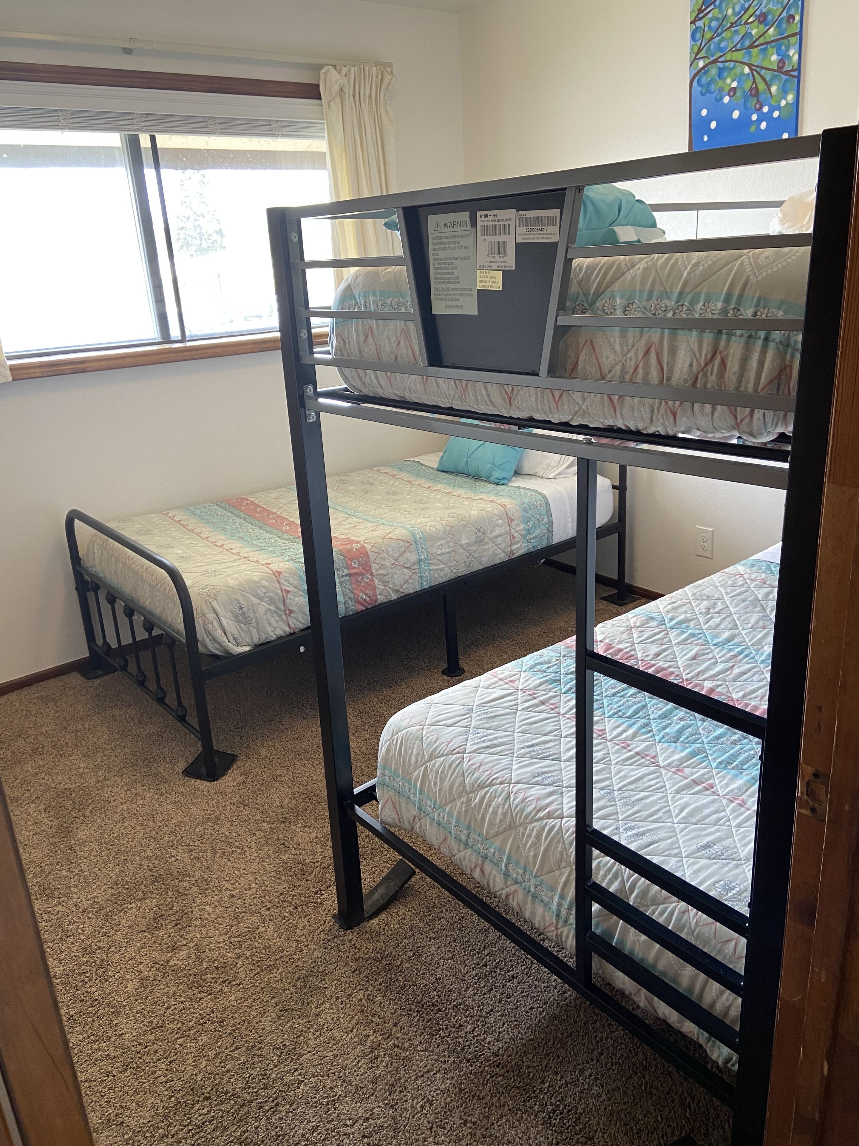 A bunk bed room with a window, carpeted floor, and a painting on the wall.