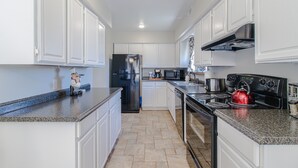 Eine moderne Küche mit weißen Schränken, Granit Arbeitsplatten, einem Edelstahl-Kühlschrank, einem roten Wasserkocher und einem Gasherd.