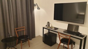 A compact room with a desk, two chairs, a television, a small refrigerator, and a coffee maker. - H hotel (Seoul)