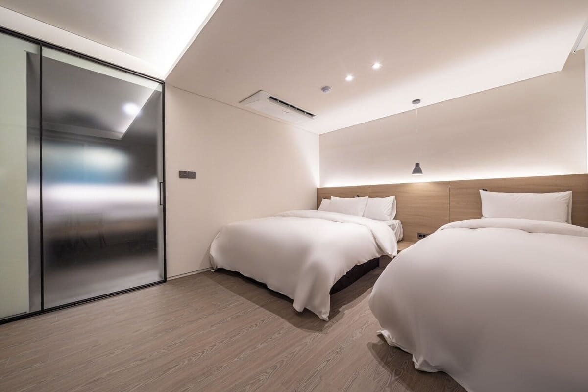A modern bedroom with two beds, a sliding glass door, and a sloped ceiling.
