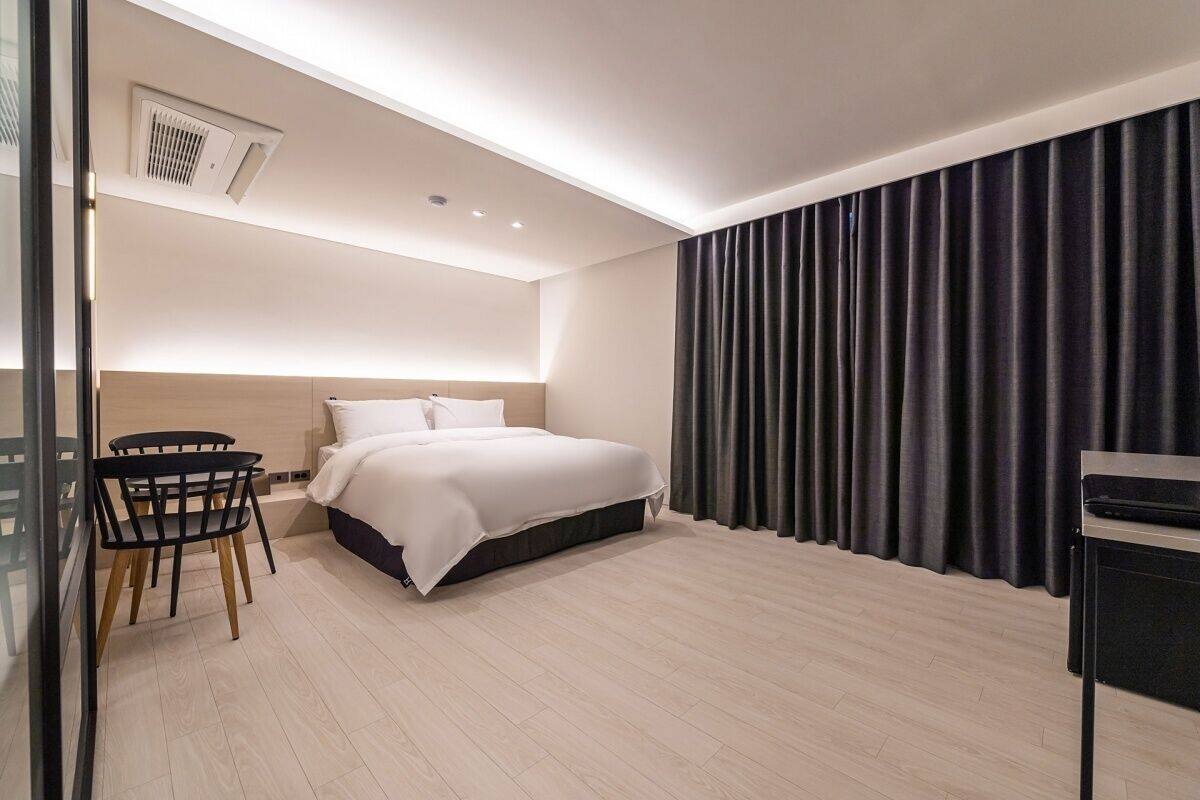 A modern hotel room with a bed, a desk, a chair, and a large window with curtains.
