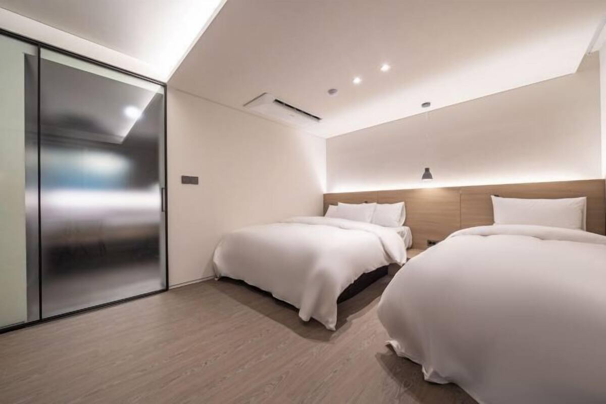 A modern hotel room with two beds, a sliding door, and a skylight.