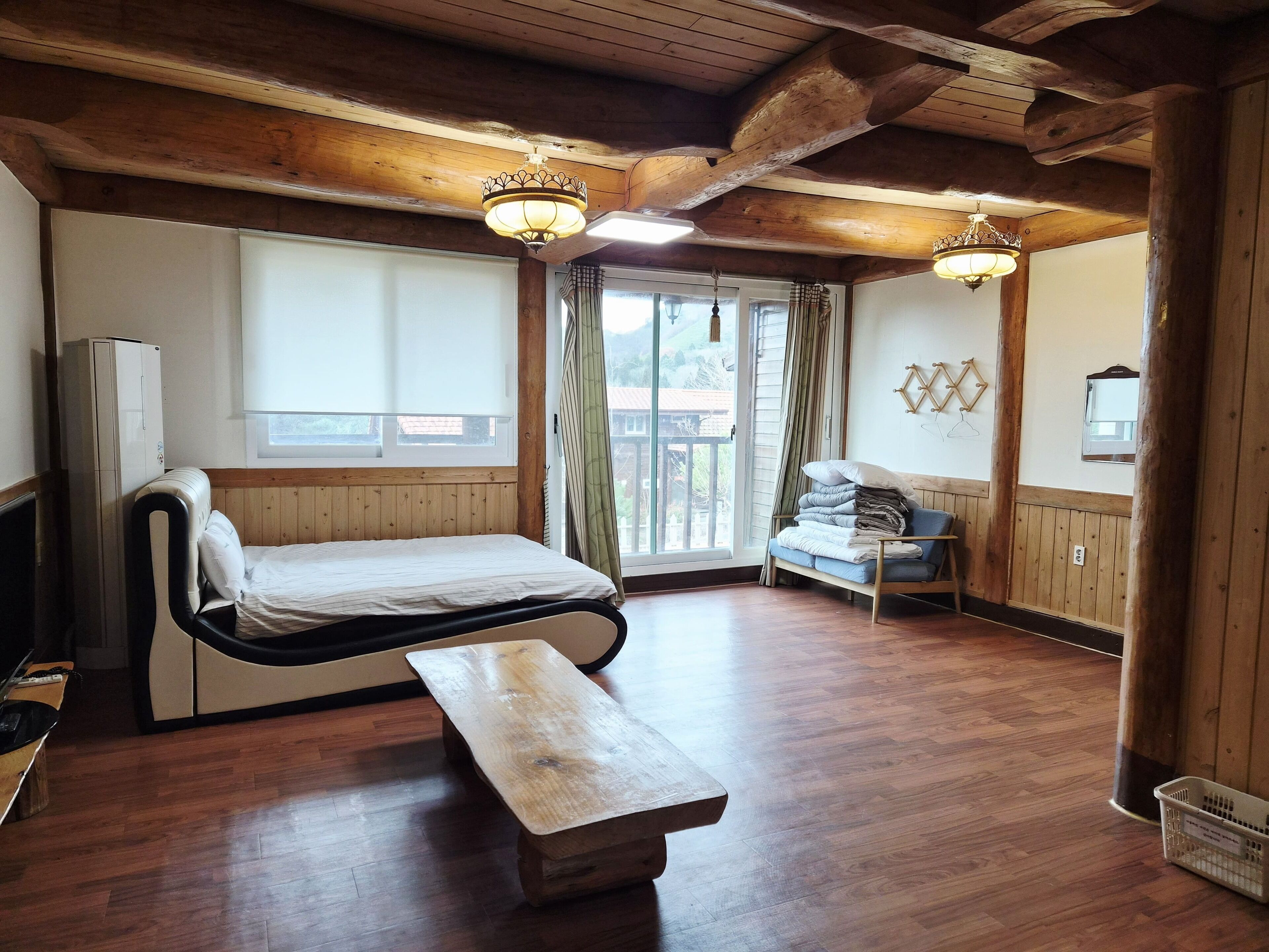 A wooden cabin-style room with a bed, bench, and a view of the outdoors.
