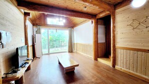 A wooden interior with a large sliding glass door leading to a deck, a wooden bench, and a television on a wooden stand.