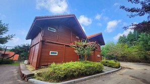A wooden cabin with a sloped roof, surrounded by greenery and a clear sky. - Nokcha Resort (Boseong)