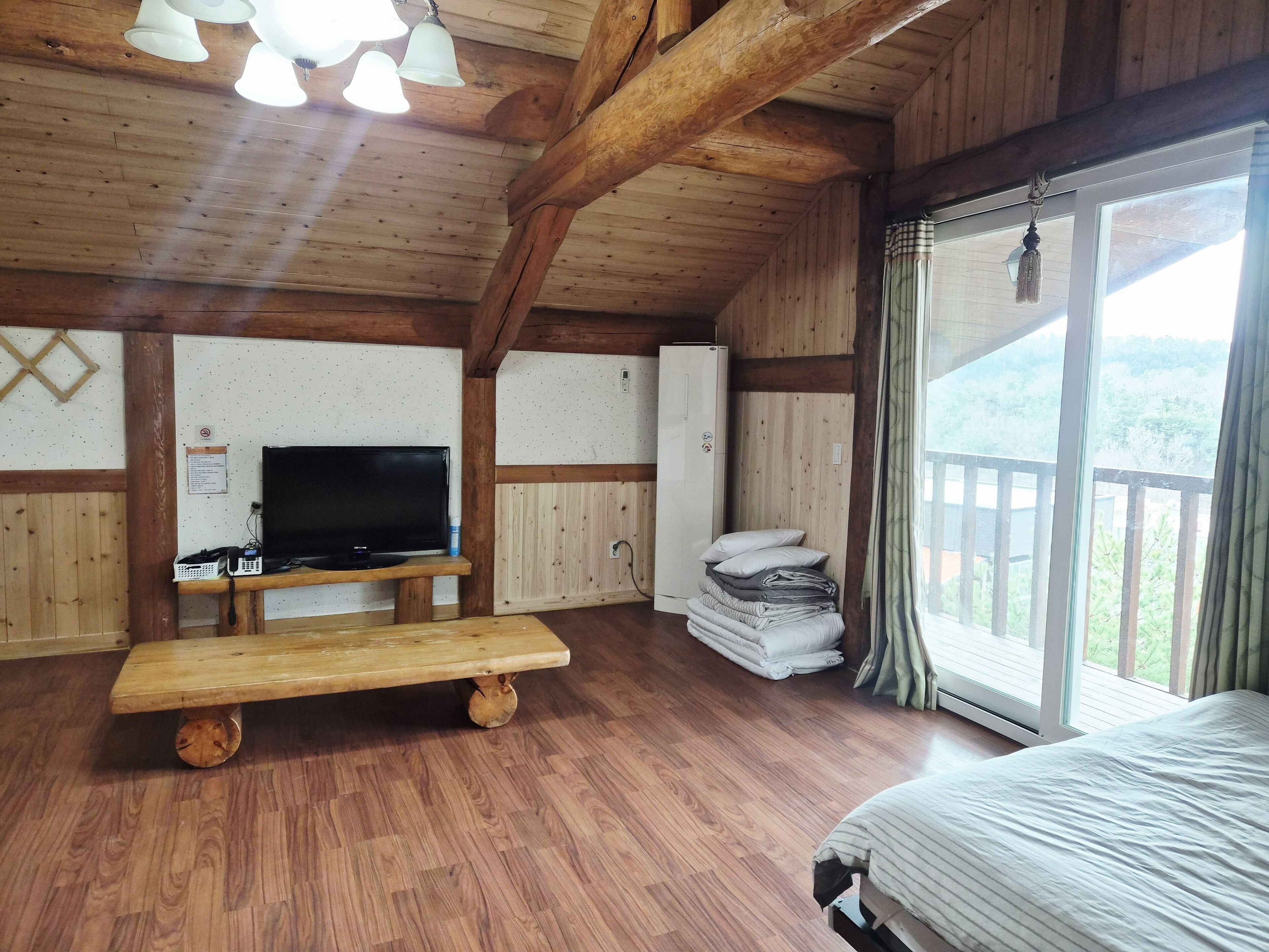 Een houten kamer met een televisie, een bank, een stapel kussens en een bed.