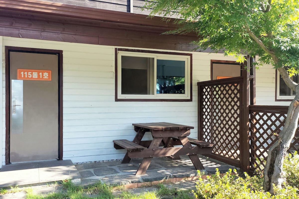 Un edificio pequeño con puerta y ventana de madera, una mesa de picnic y una cerca de madera.