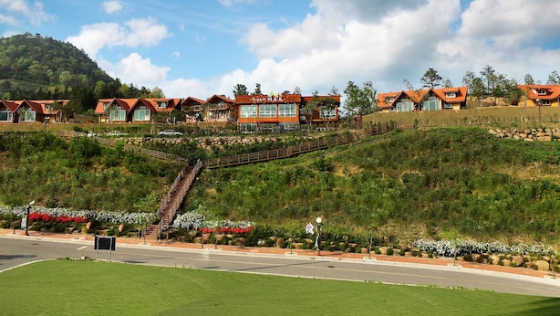 A hillside resort with multiple red-roofed buildings, a staircase leading up, and a well-maintained lawn.