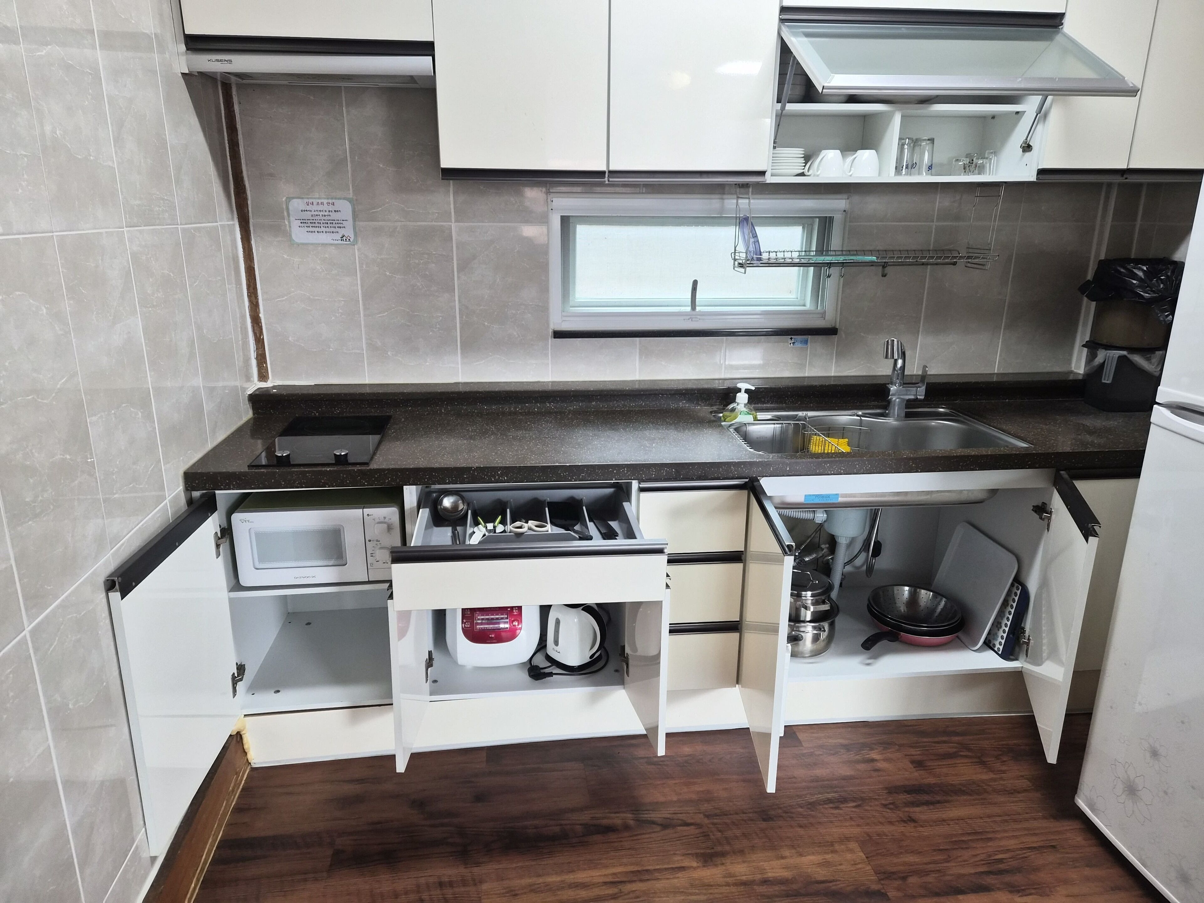 Una cocina compacta equipada con microondas, hervidor y un lavamanos pequeño.