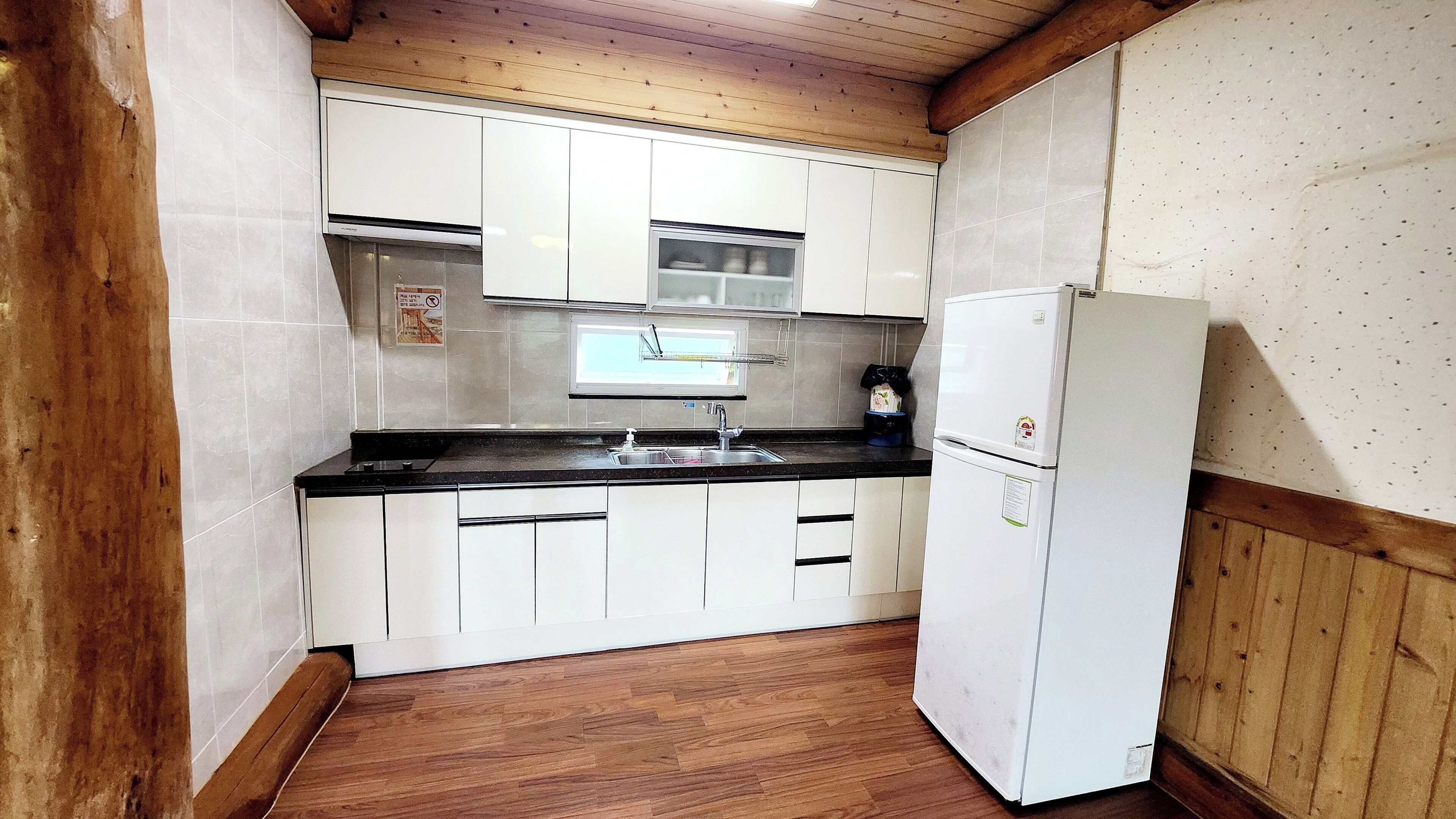 Una cocina compacta con armarios blancos, encimera negra, pileta de acero inoxidable y refrigerador blanco.