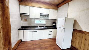 Una cocina compacta con armarios blancos, encimera negra, pileta de acero inoxidable y refrigerador blanco.