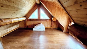 Una camera mansardata in legno con soffitto spiovente, ampie finestre e un mucchio di lenzuola bianche sul pavimento.