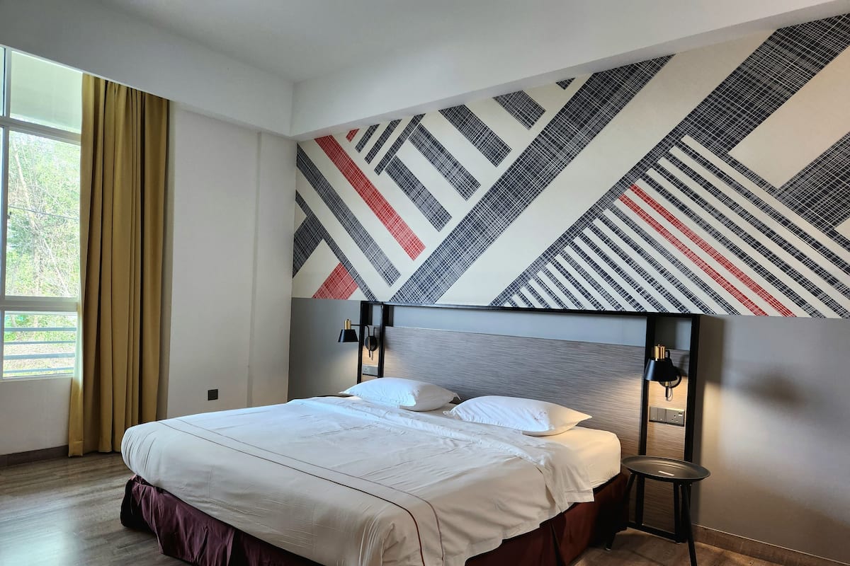 A modern hotel room with a large bed, a patterned wall, and a window with curtains.