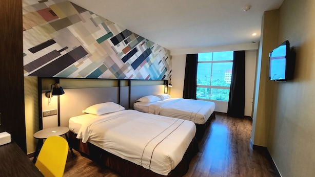 Habitación de hotel con dos camas, una mesita redonda y un ventanal con vistas a la ciudad.