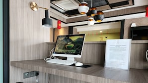Un mostrador de recepción de hotel con una computadora de escritorio, teclado y ratón. Hay lámparas fijadas a la pared y un cartel con información de la administración del hotel.